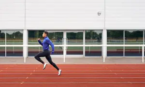 Un atleta con ropa deportiva azul y negra corre en una pista de atletismo roja, capturando la esencia de una serie running.