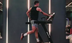 Hombre entrenando en cinta, ajustando la velocidad. El gimnasio moderno con luces LED crea un ambiente dinámico para el ejercicio.