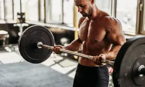 Hombre musculoso levanta barra en gimnasio. Si buscas como engordar de forma saludable, el entrenamiento de fuerza es clave.