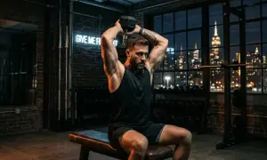 Hombre realizando ejercicio de tríceps con mancuerna en un gimnasio con vista a la ciudad.