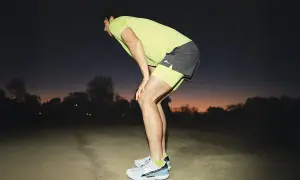 Corredor con las manos en las rodillas, recuperando el aliento al anochecer. Consejos para saber como evitar el flato al correr.