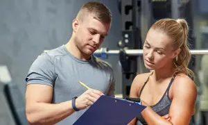 Un personal trainer que es, explica un plan de entrenamiento a una mujer en un gimnasio.