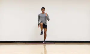 Hombre realizando ejercicio de pliometría para corredores, levantando una rodilla y extendiendo un brazo.