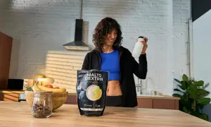 Mujer sonriente con una botella en la mano, junto a un paquete de MALTO DEXTRIN, un carbohidrato para energía.