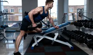 Hombre musculoso haciendo remo inclinado con mancuerna en un gimnasio.