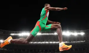 Pedro Pablo Pichardo en pleno salto triple, demostrando su potencia y técnica en el aire, con el estadio iluminado de fondo.