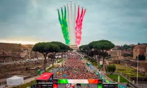 La **media maratón Roma** comienza con aviones dibujando la bandera italiana en el cielo, sobre una multitud de corredores y el Coliseo al fondo.