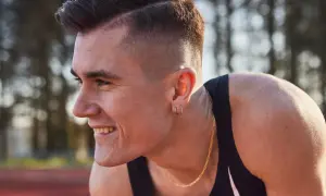 Un atleta sonríe, con su corte de pelo moderno y un collar dorado. Podría ser uno de los hermanos Ingebrigtsen, listo para competir.