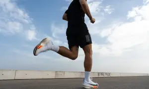 Un corredor con zapatillas blancas y naranjas practica como correr correctamente bajo un cielo azul con nubes.
