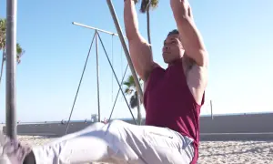 Hombre haciendo abdominales en barra en la playa, con palmeras y el mar de fondo.