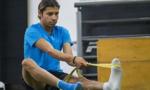 Luis Grijalva estira sus piernas con una banda de resistencia amarilla, preparándose para el entrenamiento.
