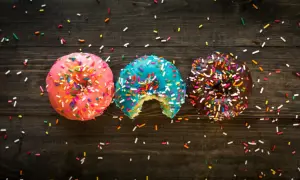 Tres donas coloridas con chispas, una mordida en la azul. ¡Un festín visual que desafía la dieta inversa!