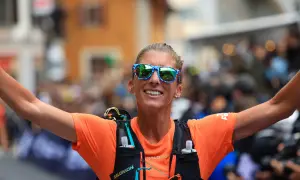 Courtney Dauwalter, con gafas de sol llamativas y camiseta naranja, celebra con los brazos extendidos tras una carrera.