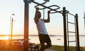 Hombre entrenando en barra exterior, aprendiendo como hacer dominadas al atardecer.