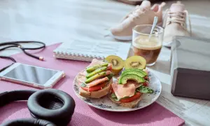Dos sándwiches con aguacate y jamón serrano, ideales para que picar entre horas saludable. Junto a unas zapatillas deportivas y café.