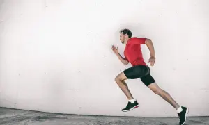 Corredor en pleno entrenamiento maratón, con ropa deportiva roja y negra, contra una pared de hormigón.