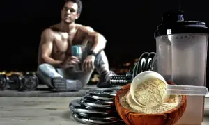 Un hombre musculoso descansa con pesas y un batido. El ácido aspártico para qué sirve: ayuda en la recuperación muscular y la energía.