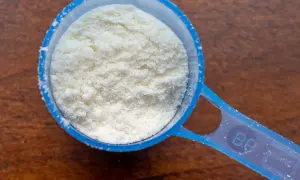 Cuchara dosificadora azul llena de polvo blanco, quizás proteína en polvo. ¿Tomar proteínas es malo?