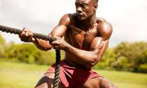 Hombre musculoso en entrenamiento espartano, tirando de una cuerda con fuerza.