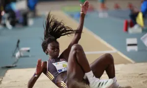 Atleta en pleno salto de longitud femenino, aterrizando en la arena con el cabello al viento.