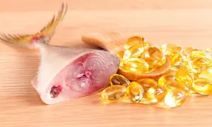 Un trozo de pescado fresco junto a cápsulas doradas, representando los **aceite de hígado de bacalao beneficios** para la salud.