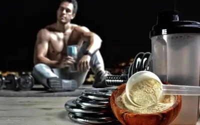 Un hombre musculoso descansa con pesas y un batido. El ácido aspártico para qué sirve: ayuda en la recuperación muscular y la energía.