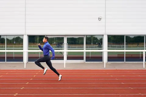 Un atleta con ropa deportiva azul y negra corre en una pista de atletismo roja, capturando la esencia de una serie running.