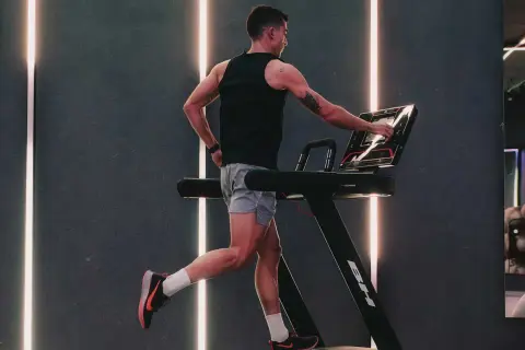 Hombre entrenando en cinta, ajustando la velocidad. El gimnasio moderno con luces LED crea un ambiente dinámico para el ejercicio.