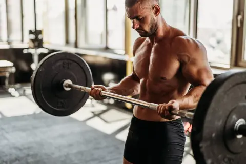 Hombre musculoso levanta barra en gimnasio. Si buscas como engordar de forma saludable, el entrenamiento de fuerza es clave.