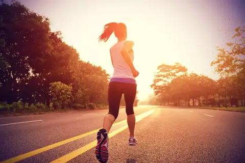 Mujer corriendo por una carretera al atardecer, entrenando para la distancia media maratón.