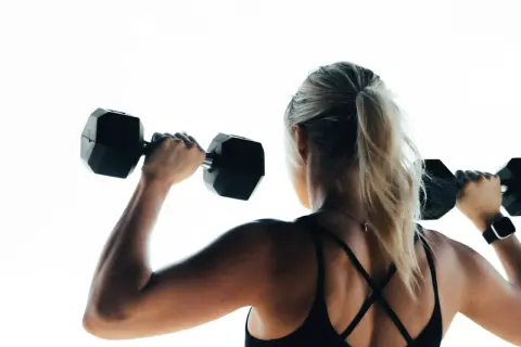 Mujer rubia con coleta levanta pesas negras. Su espalda muestra la fuerza que un vegano puede tener.