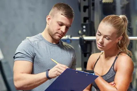 Un personal trainer que es, explica un plan de entrenamiento a una mujer en un gimnasio.