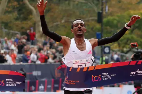 Tamirat Tola cruza la meta de la Maratón de Nueva York, victorioso, con los brazos en alto.