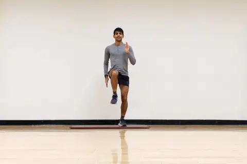 Hombre realizando ejercicio de pliometría para corredores, levantando una rodilla y extendiendo un brazo.