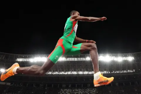 Pedro Pablo Pichardo en pleno salto triple, demostrando su potencia y técnica en el aire, con el estadio iluminado de fondo.