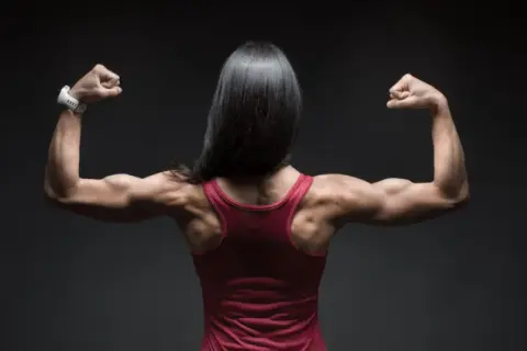 Mujer con espalda musculosa y brazos flexionados, mostrando su fuerza. El óxido nítrico para qué sirve: potencia el rendimiento deportivo.