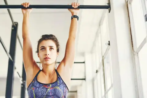 Mujer concentrada haciendo dominadas, un ejercicio clave para obtener grandes beneficios.