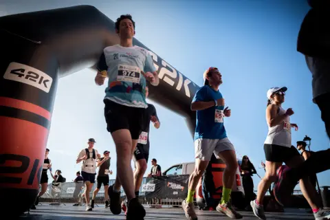 Corredores cruzan la meta de la media maratón bajo un arco inflable. El dorsal 974 destaca en un participante.