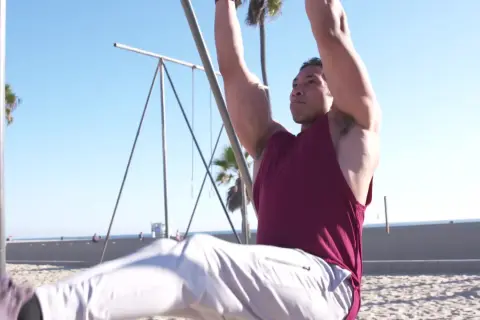 Hombre haciendo abdominales en barra en la playa, con palmeras y el mar de fondo.