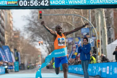 Atleta cruza la meta, celebrando su victoria y un posible récord de 1500 metros. El cronómetro marca 00:56:42.