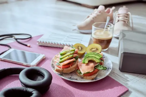 Dos sándwiches con aguacate y jamón serrano, ideales para que picar entre horas saludable. Junto a unas zapatillas deportivas y café.
