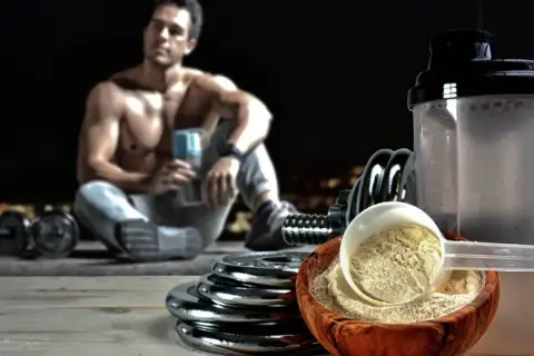 Un hombre musculoso descansa con pesas y un batido. El ácido aspártico para qué sirve: ayuda en la recuperación muscular y la energía.