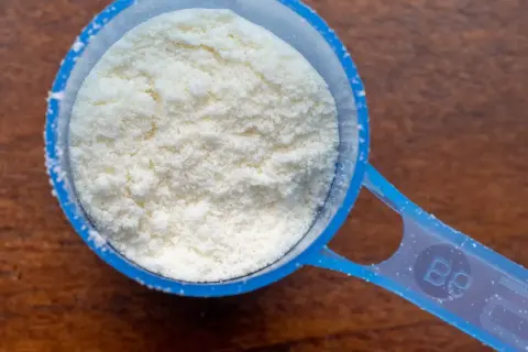 Cuchara dosificadora azul llena de polvo blanco, quizás proteína en polvo. ¿Tomar proteínas es malo?