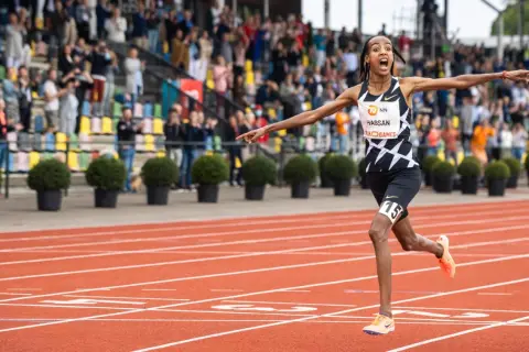 Sifan Hassan cruza la meta en un maratón, con los brazos extendidos y una expresión de júbilo.