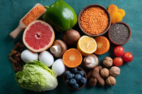 Variedad de alimentos alcalinos lista: lentejas, pomelo, pimiento verde, champiñones, limón, naranjas, tomates, arándanos, huevos, lechuga, pasta integral, semillas de chía, nueces y tamarindos.