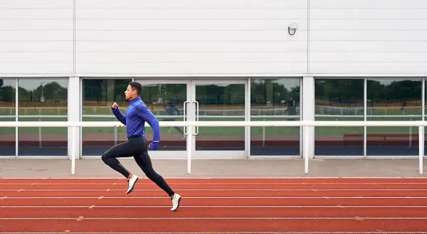 Un atleta con ropa deportiva azul y negra corre en una pista de atletismo roja, capturando la esencia de una serie running.