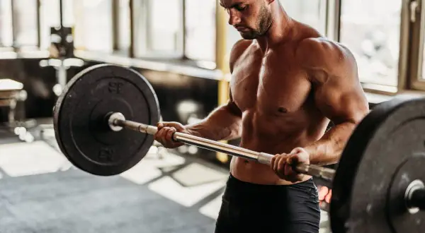 Hombre musculoso levanta barra en gimnasio. Si buscas como engordar de forma saludable, el entrenamiento de fuerza es clave.