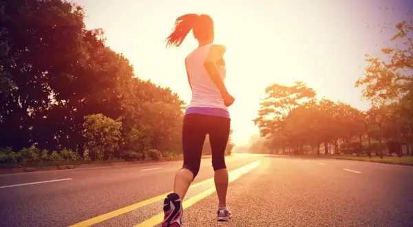 Mujer corriendo por una carretera al atardecer, entrenando para la distancia media maratón.
