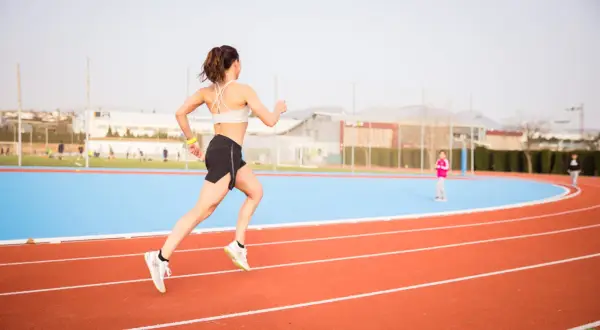 Mujer corriendo en pista de atletismo, lista para las noticias running.