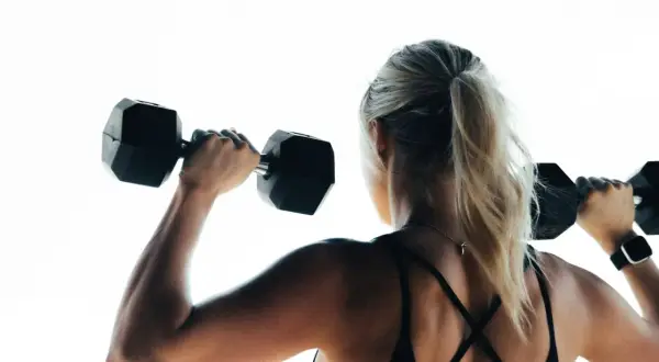 Mujer rubia con coleta levanta pesas negras. Su espalda muestra la fuerza que un vegano puede tener.